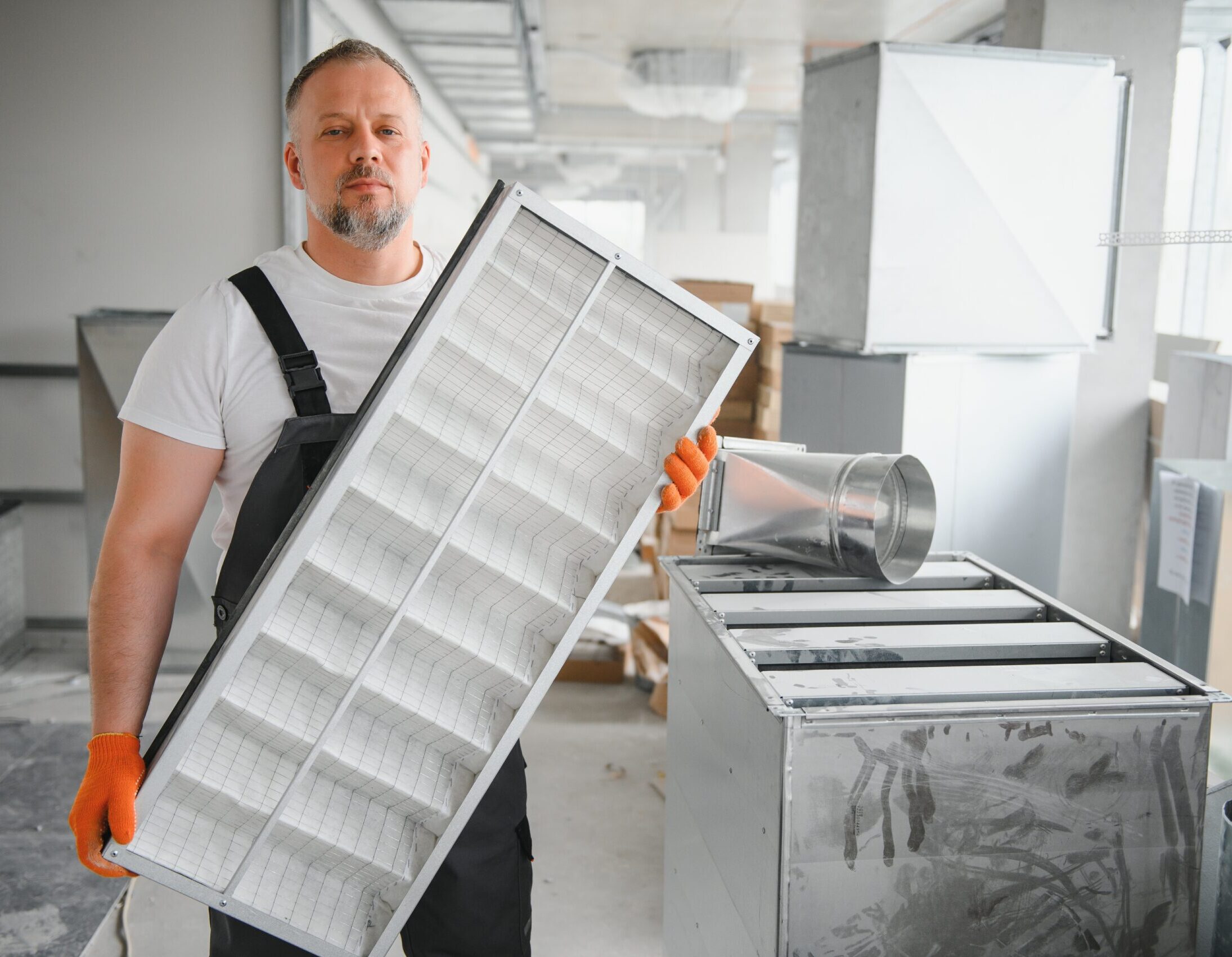 A male worker holds an air filter for air conditioning in an office space. Installation of an air conditioner